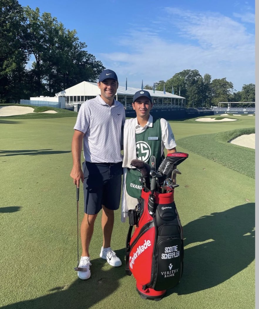 An Evans Scholar in a green ES caddie bib on the green at a PGA TOUR event, beside the player whose bag he carried.